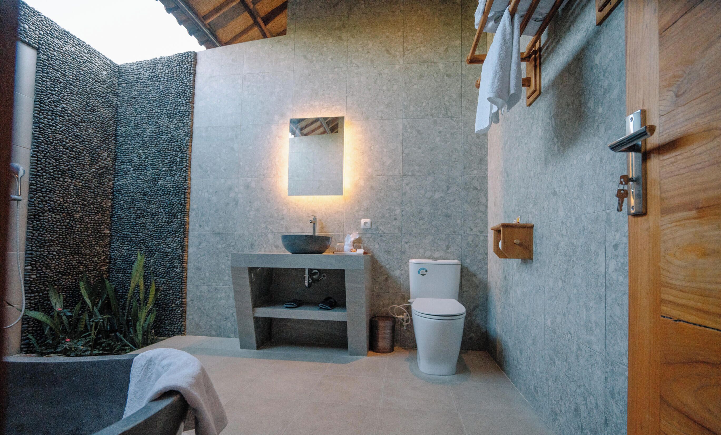 Een compacte badkamer met een stenen muur, een wastafel, toilet en een houten deur.