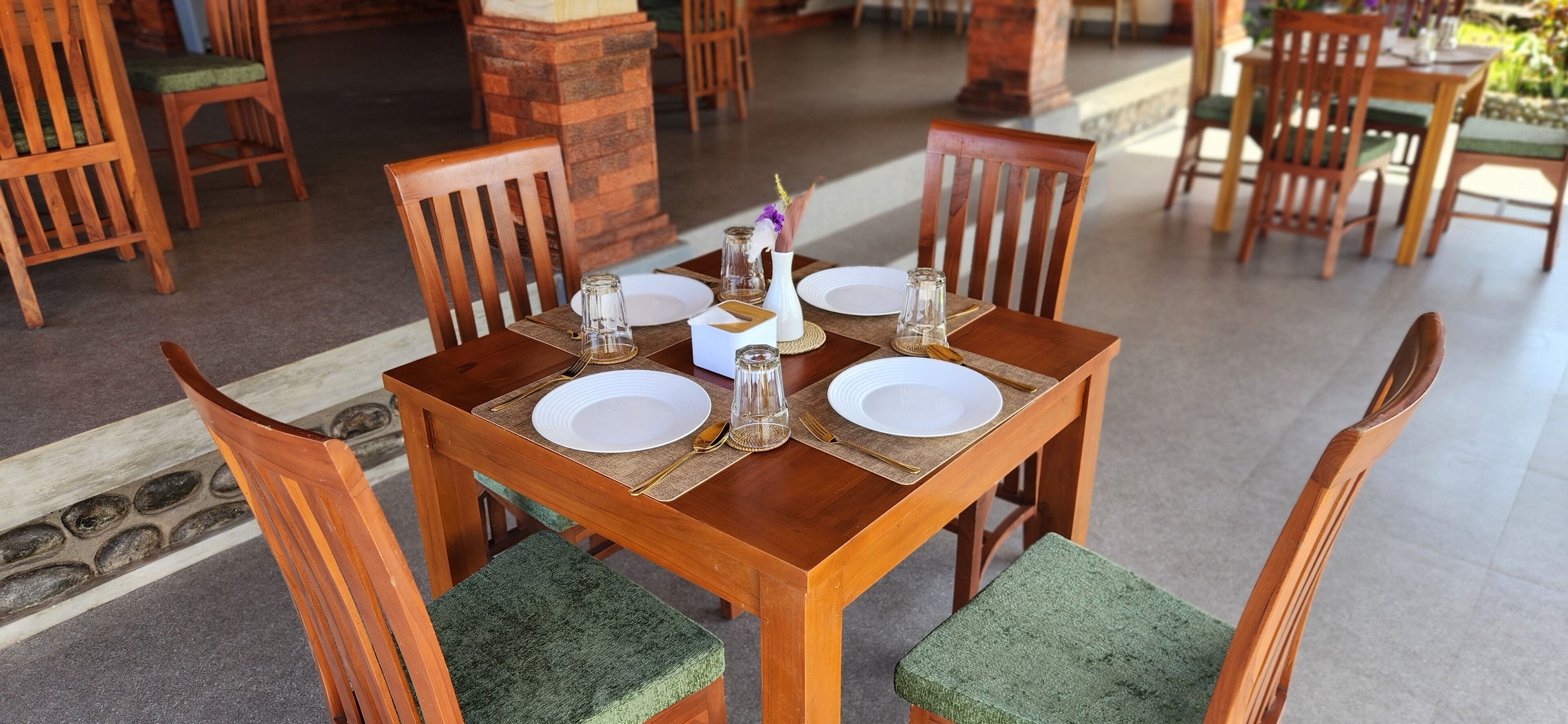 A wooden dining table with four chairs, each with a green cushioned seat. The table is set with white plates, cutlery, and glassware.