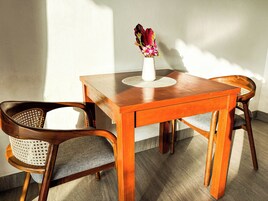 Una mesa de comedor de madera con un jarrón de flores, dos sillas tapizadas y un mantel tejido.