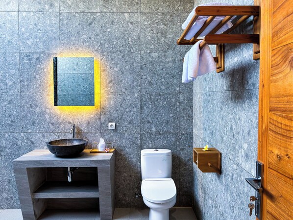A bathroom with a stone sink, a white toilet, and a wooden towel rack. - Terrace Retreat & Spa (Pekutatan)