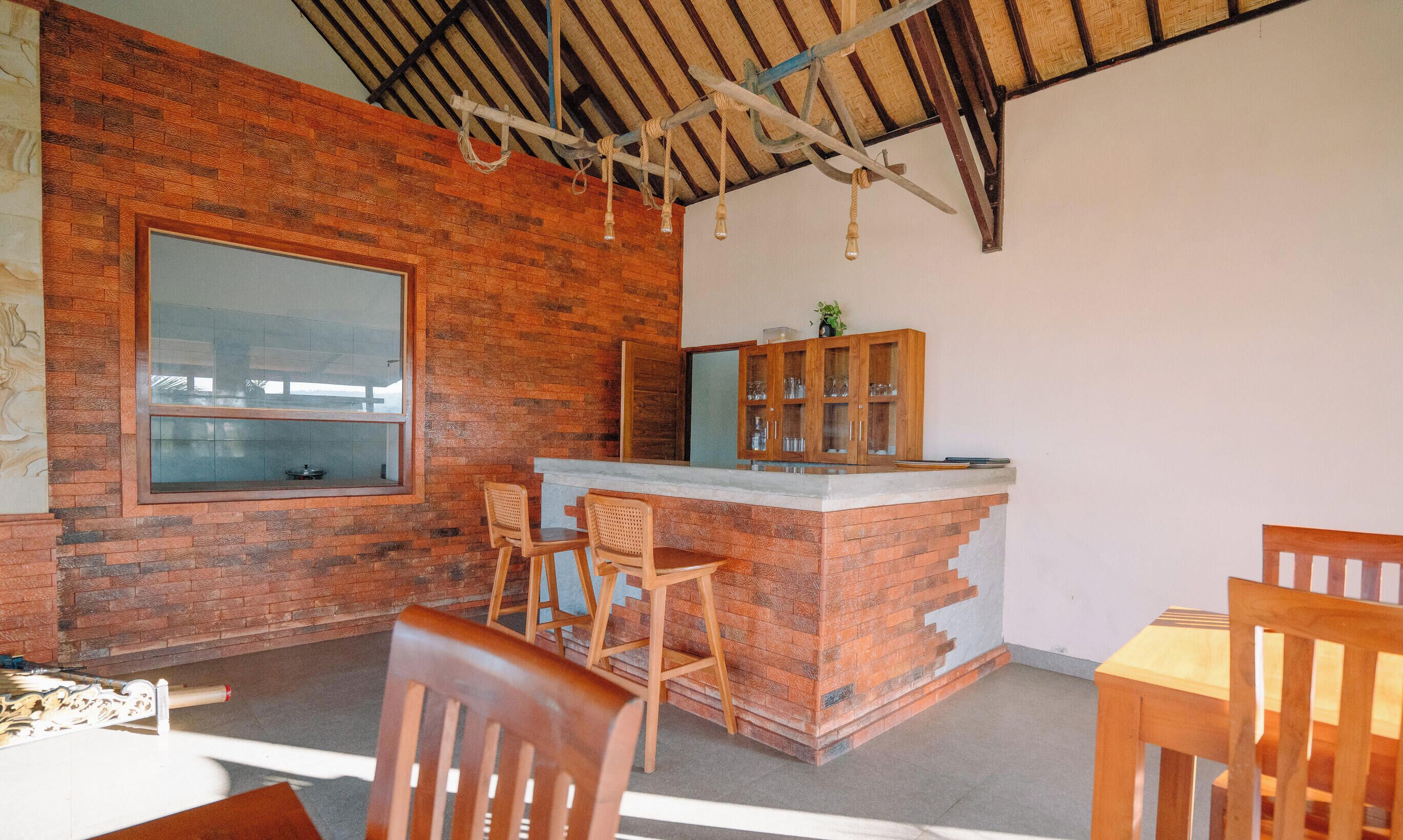 Un interior rústico con pared de ladrillo, una ventana grande, una barra de madera y una zona de comedor con sillas.