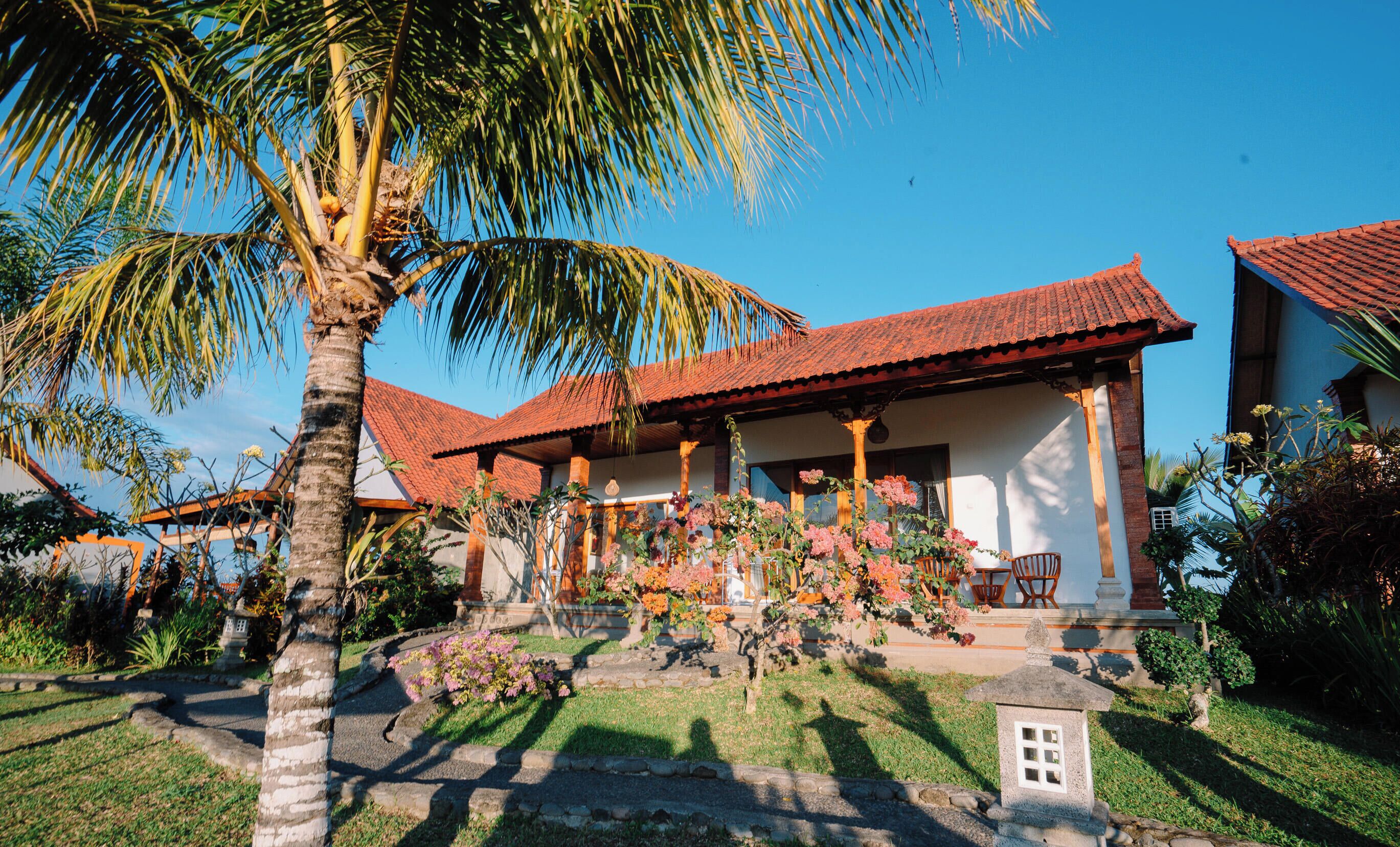 A traditional house with a red-tiled roof, surrounded by lush greenery and flowering plants.