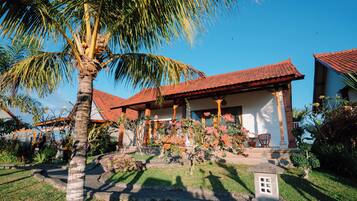 A traditional house with a red-tiled roof, surrounded by lush greenery and flowering plants.