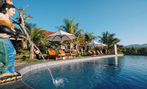 A pool area with lounge chairs and umbrellas, surrounded by palm trees and a clear sky. - Terrace Retreat & Spa (Pekutatan)