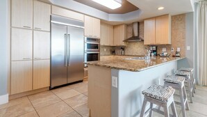 A modern kitchen with a stainless steel refrigerator, built-in oven, and a large island with bar stools. - Four Bedroom Condo with Panoramic Views and Large Wraparound Balcony. Complimentary Boat Slip! (Orange Beach)