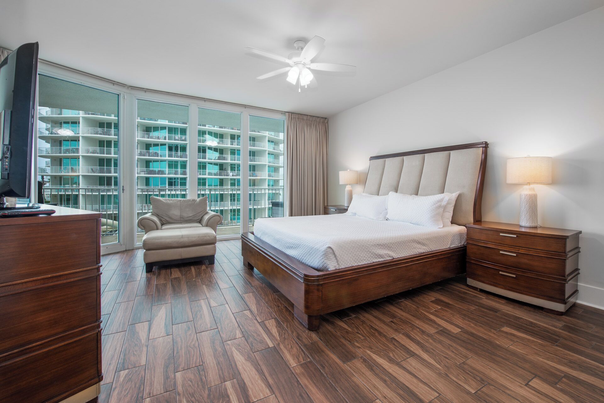 Habitación de hotel con una cama grande, un escritorio, una silla y vista a un edificio a través de amplios ventanales.