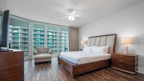 A hotel room with a large bed, a desk, a chair, and a view of a building through large windows. - Cozy Three Bedroom Poolside Condo. Complimentary Boat Slip! (Orange Beach)