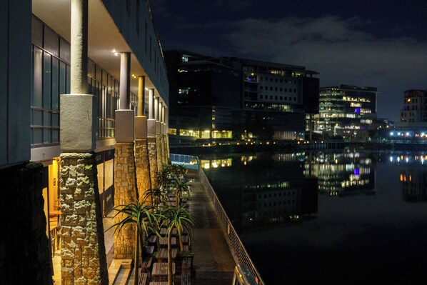 A waterfront hotel with a balcony, stone pillars, and a reflection of buildings in the water.