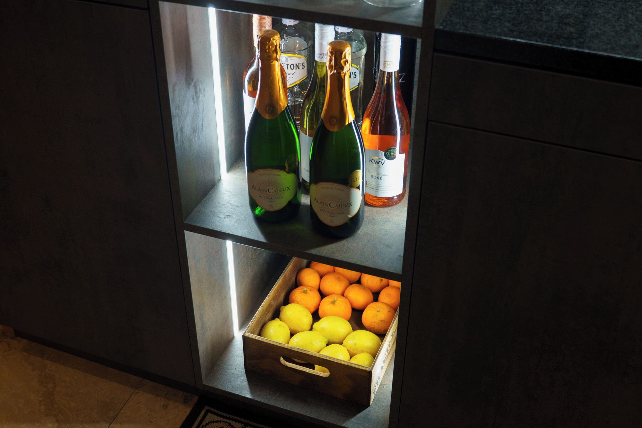 A refrigerator with bottles and a box of oranges.