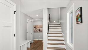 Een moderne trap met houten treden en een zwarte leuning, die leidt naar een kamer met een bank en een schilderij aan de muur.