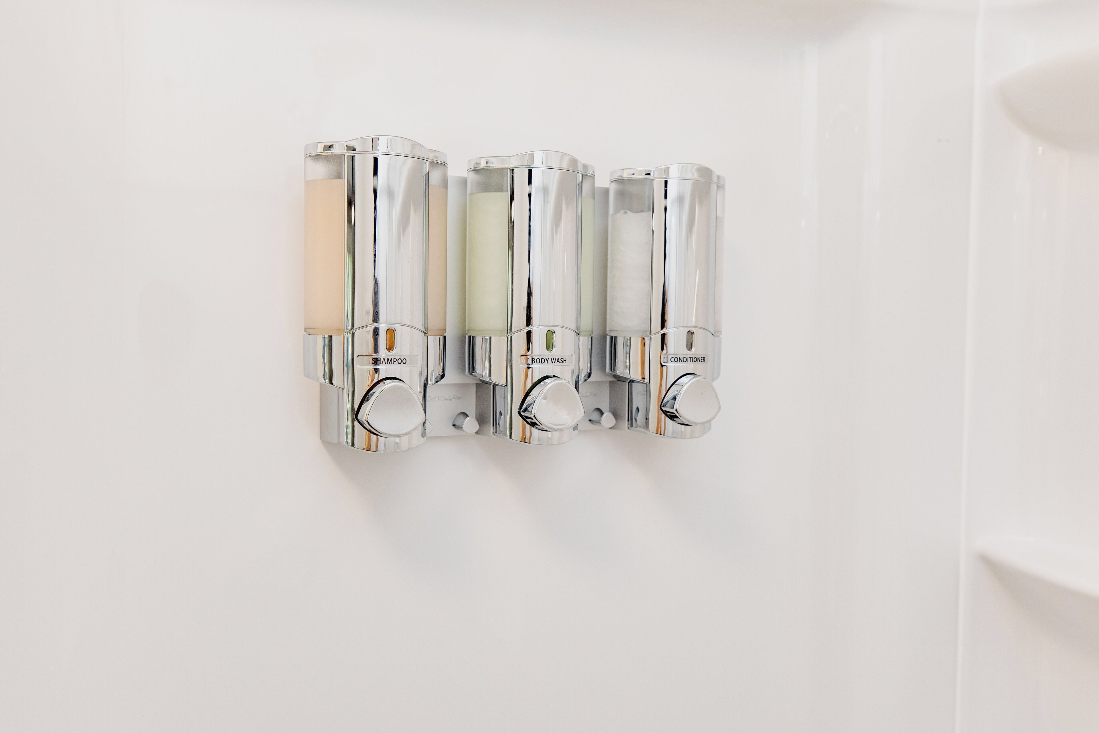 A wall-mounted dispenser with shampoo, body wash, and conditioner bottles.