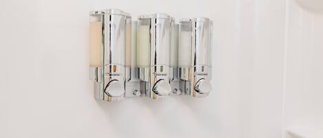 A wall-mounted dispenser with shampoo, body wash, and conditioner bottles.