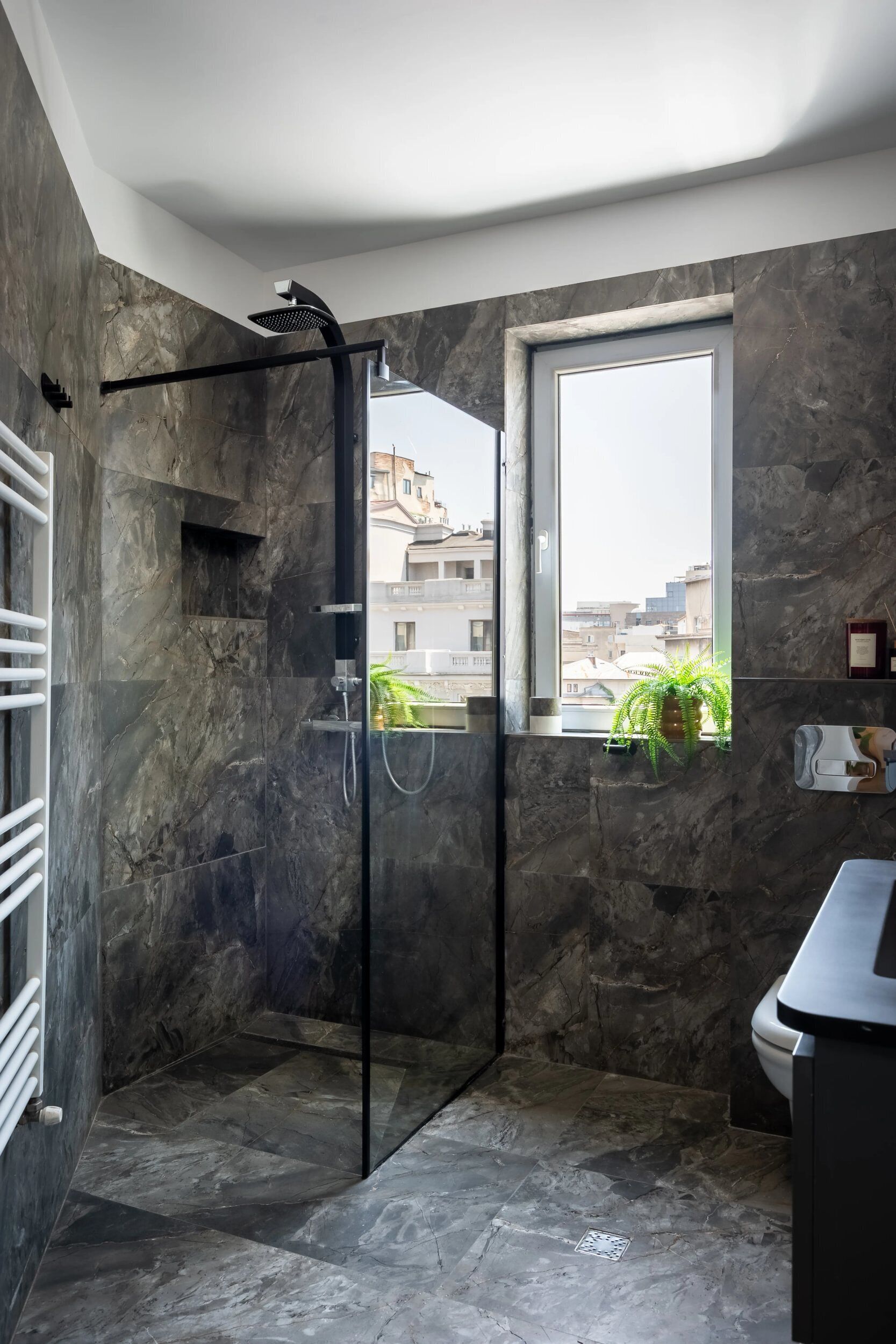 Un baño moderno con ducha de vidrio, paredes de mármol, un ventanal con vistas y un inodoro.