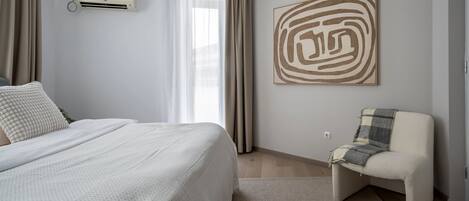 A bedroom with a bed, a chair, a wall-mounted air conditioner, and a large abstract painting.