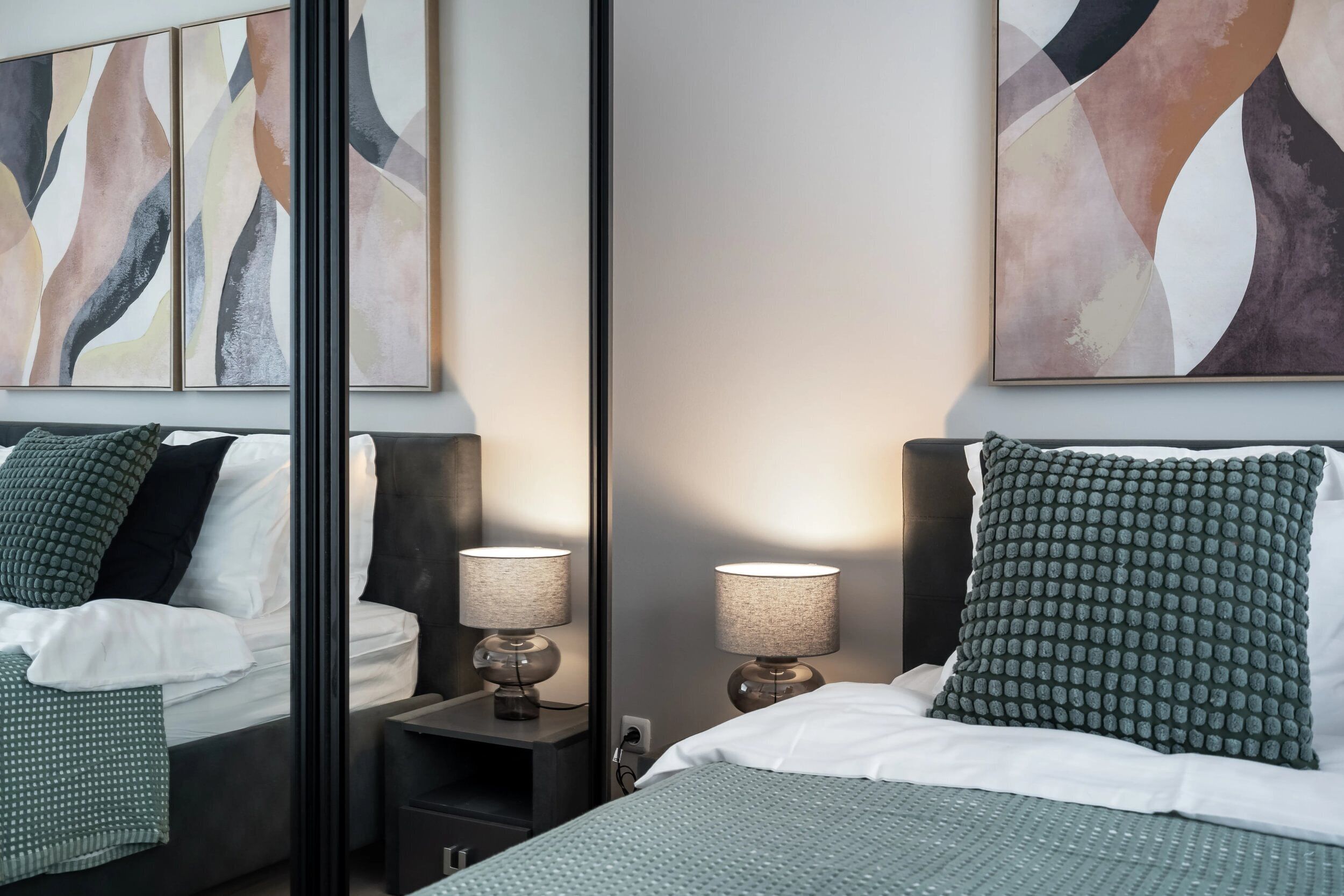 Habitación de hotel con cama, dos mesitas de noche, un espejo y un cuadro abstracto en la pared.