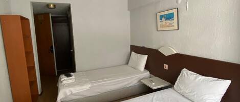 Habitación de hotel con dos camas individuales, piso de madera, pared blanca, un cuadro enmarcado y una puerta que da a otra habitación.