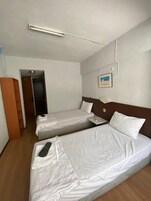 A hotel room with two single beds, a wooden floor, a white wall, a framed picture, and a door leading to another room.