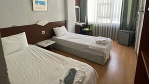 A hotel room with two beds, a desk, a chair, a small table, a mirror, and a window with curtains. - Masal Otel (Burhaniye)
