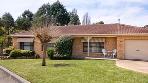 A single-story brick house with a red-tiled roof, a garage, and a small front yard with two white chairs and a tree. - 🏁 Racetrack – Charming Family Home Near Mount Panorama (South Bathurst)