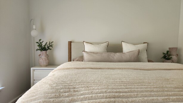 A neatly made bed with a textured blanket, a bedside lamp, and a small potted plant on a nightstand. - 🏁 Racetrack – Charming Family Home Near Mount Panorama (South Bathurst)