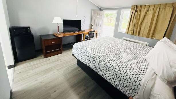 A hotel room with a bed, a desk with a computer, a television, and a microwave.