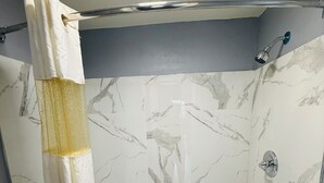 A bathroom with a bathtub, shower curtain, and marble wall tiles.