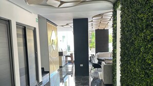 A modern lobby with a polished marble floor, a geometric ceiling design, and a green hedge wall.