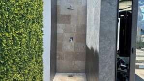 A modern outdoor shower area with a stone wall and a green hedge.