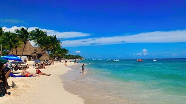A beach with clear turquoise water, palm trees, and beachgoers.