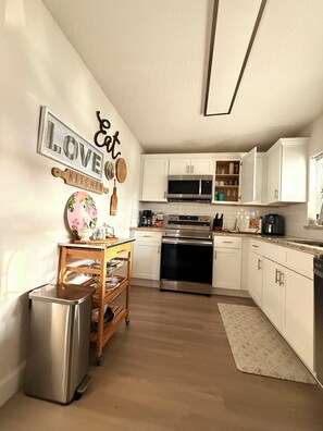 Una cocina moderna con armarios blancos, electrodomésticos de acero inoxidable y detalles decorativos en la pared.