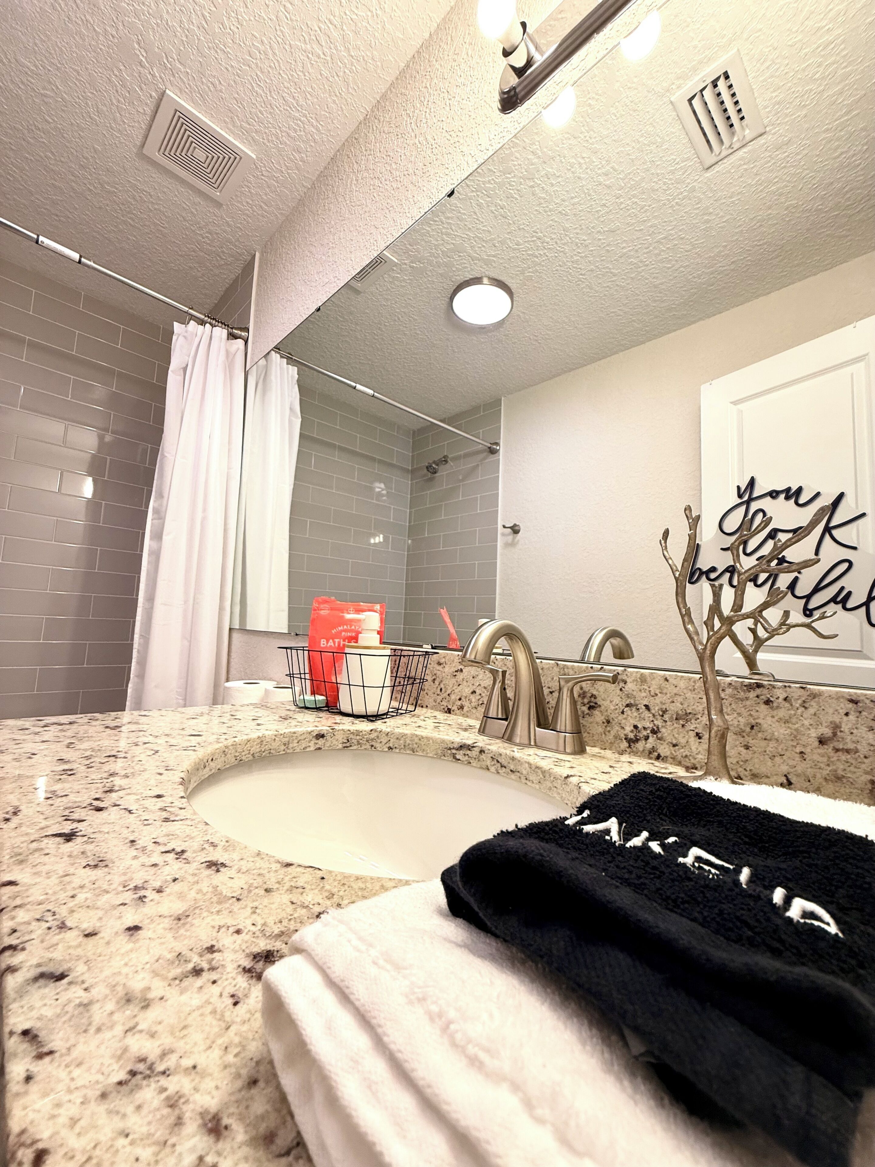 A bathroom with a granite countertop sink, a mirror, a shower with a curtain, and a towel rack.