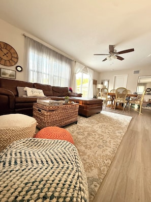 A living room with a brown sofa, a coffee table, and a dining area with chairs and a table.