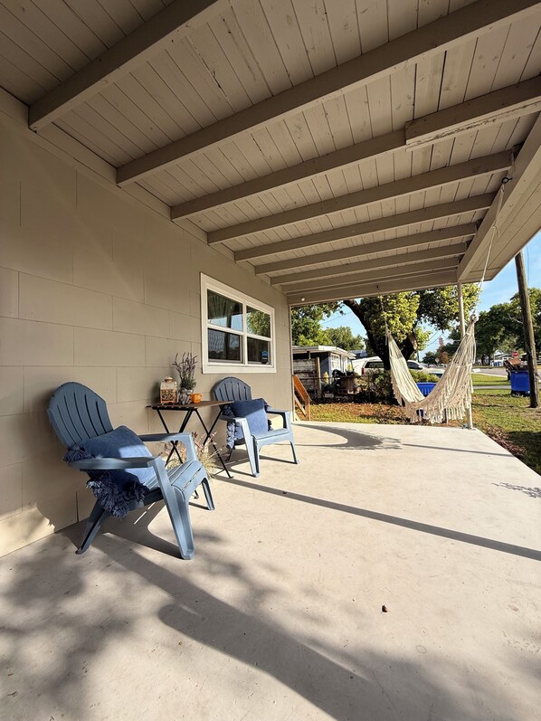 A covered patio with two chairs, a table, and a hammock.