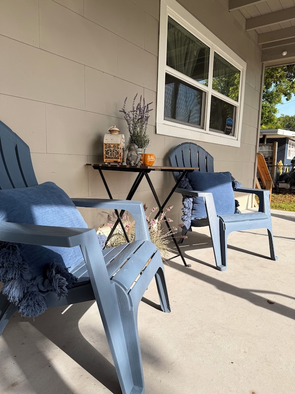 Eine Veranda mit zwei blauen Adirondack-Stühlen, einem kleinen Tisch mit Dekoration und einem Fenster mit Blick ins Freie.