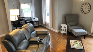 A modern living room with a leather sofa, a small table with a basket, a grey armchair, and a clock on the wall.