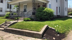 A two-story house with a covered porch, a front yard with a small garden, and a concrete planter.