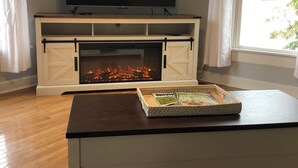 A living room with a fireplace, a flat-screen TV mounted above it, and a magazine on a table.