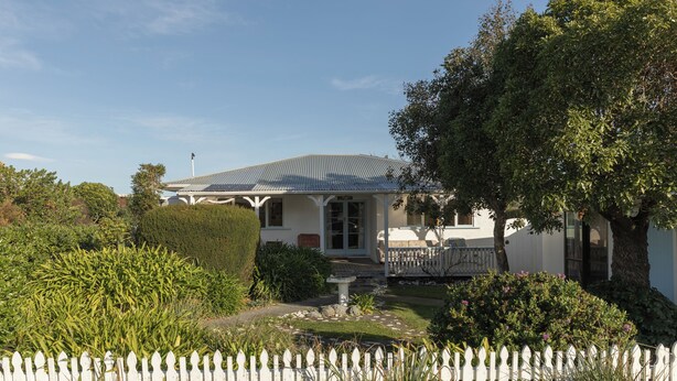 Une maison blanche avec un porche et un jardin à l’avant.