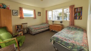 Une chambre avec deux lits simples, un fauteuil vert, une commode en bois et une bibliothèque.