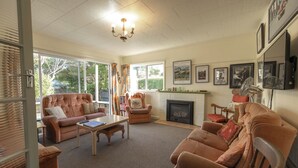 Un salon chaleureux avec une cheminée, des fauteuils confortables et de grandes fenêtres.