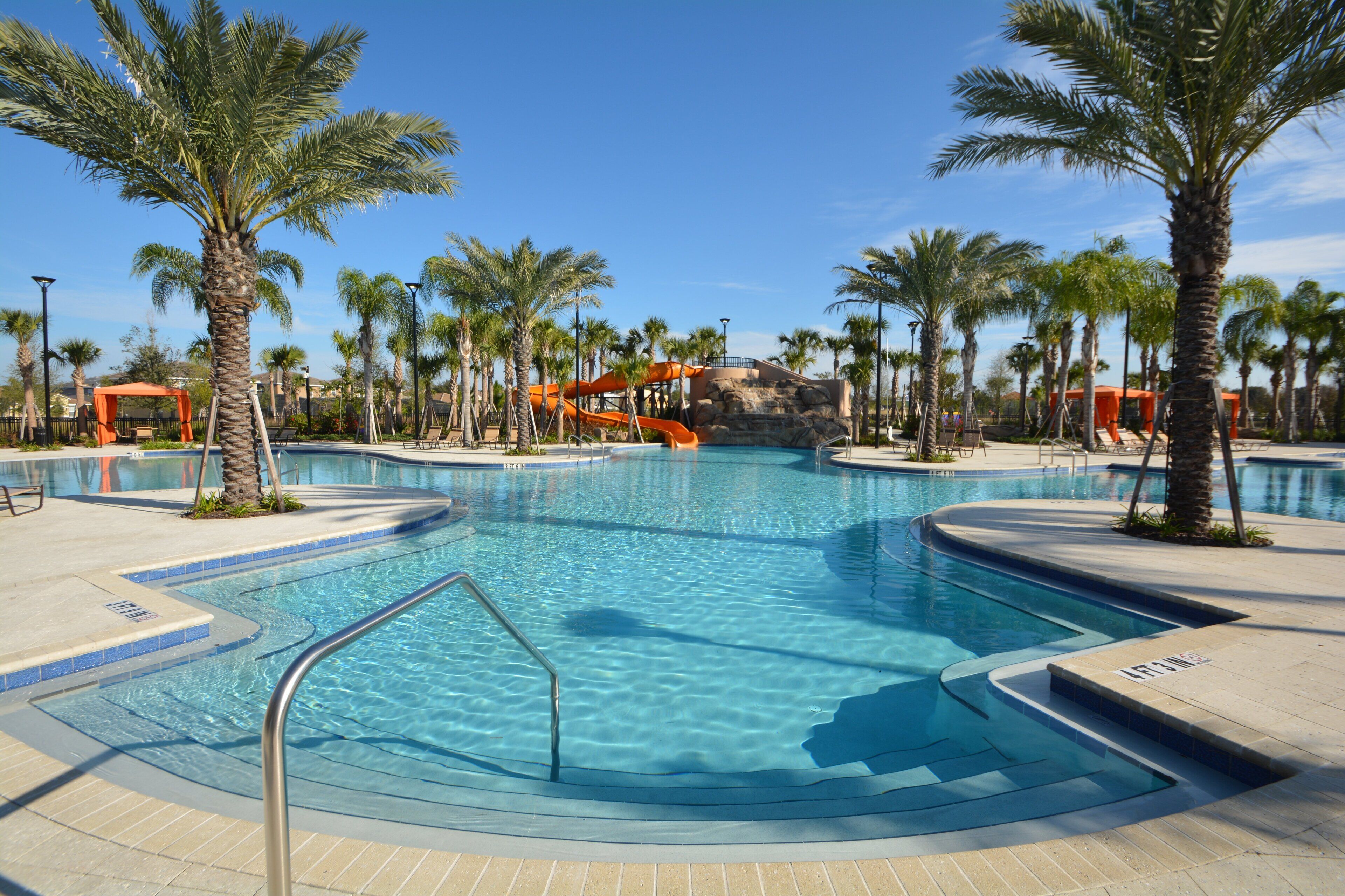 A swimming pool with a water slide, palm trees, and a clear blue sky.