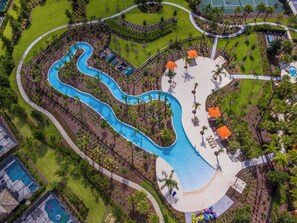 Una vista aerea di un resort con una piscina sinuosa, palme e aree salotto all'aperto.