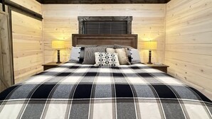 A bedroom with a plaid bedspread, wooden walls, a wooden headboard, two bedside lamps, and a window with blinds. - 33 MI to YNP | Wifi | Reservoir Access (Island Park)