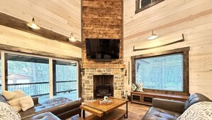 A spacious living room with a stone fireplace, leather sofas, and large windows offering views of the outdoors. - 33 MI to YNP | Wifi | Reservoir Access (Island Park)