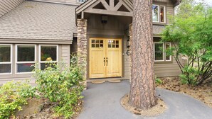 A two-story house with a stone foundation, a large tree in front, and a front door with a window above it. - 4 Red Fir - Ultimate Sunriver Stay, Game Room, Hot Tub, Walk to SHARC, Passes Included (Sunriver)
