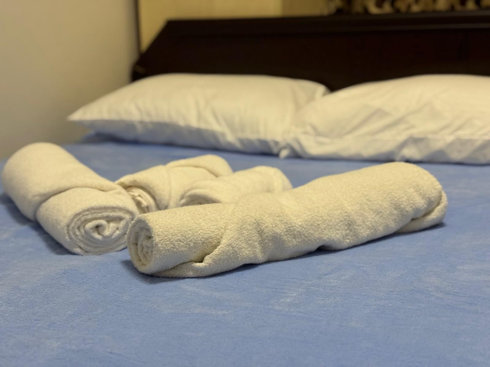 A bed with blue sheets and two rolled white towels on it.
