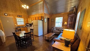 A cozy cabin interior with a wooden dining table, chairs, a sofa, a coffee table, a lamp, and a kitchen area with a refrigerator and microwave. - Southern Charm Sardis cabin 2-bedrooms with A/C, WiFi, and satellite TV (Sardis)