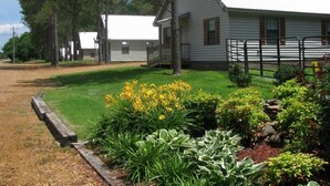 A white building with a sloped roof, surrounded by a well-maintained lawn and garden with yellow flowers. - Southern Charm Sardis cabin 2-bedrooms with A/C, WiFi, and satellite TV (Sardis)