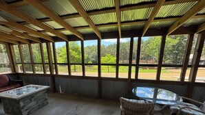 A covered outdoor seating area with a glass table and wicker chairs, overlooking a green landscape. - Southern Charm Sardis cabin 2-bedrooms with A/C, WiFi, and satellite TV (Sardis)