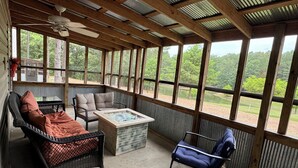 A covered patio with wicker furniture, a glass-top table, and a view of a wooded area. - Southern Charm Sardis cabin 2-bedrooms with A/C, WiFi, and satellite TV (Sardis)